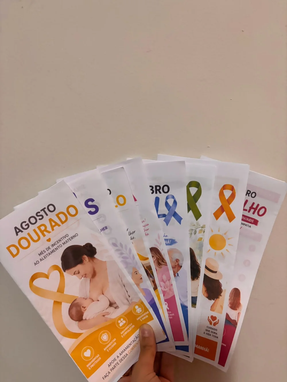 Folders impressos segurados em leque, com o Agosto Dourado à frente