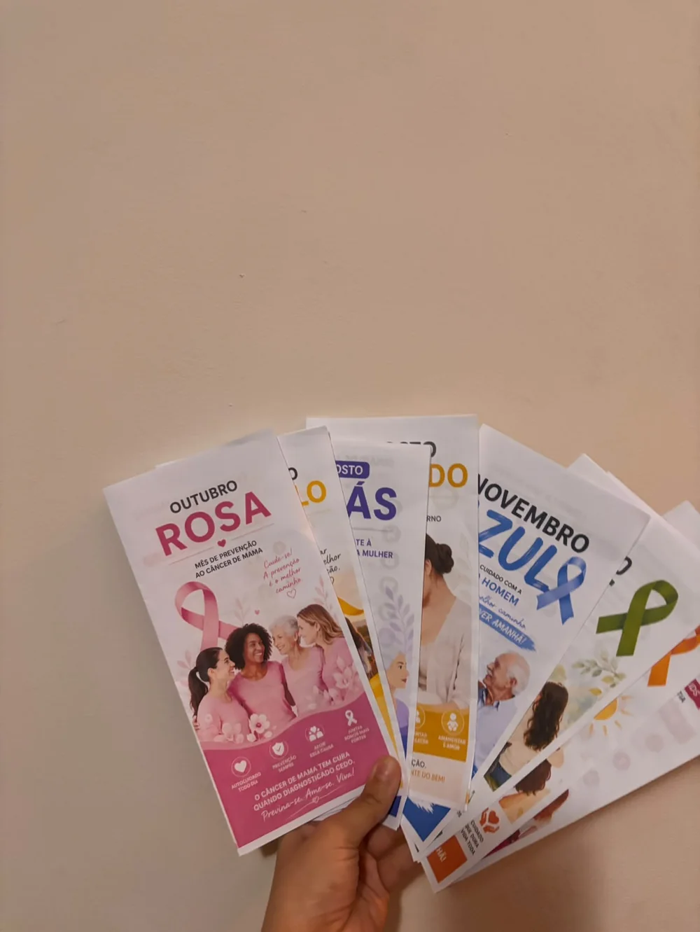 Folders impressos segurados em leque, com o Outubro Rosa à frente